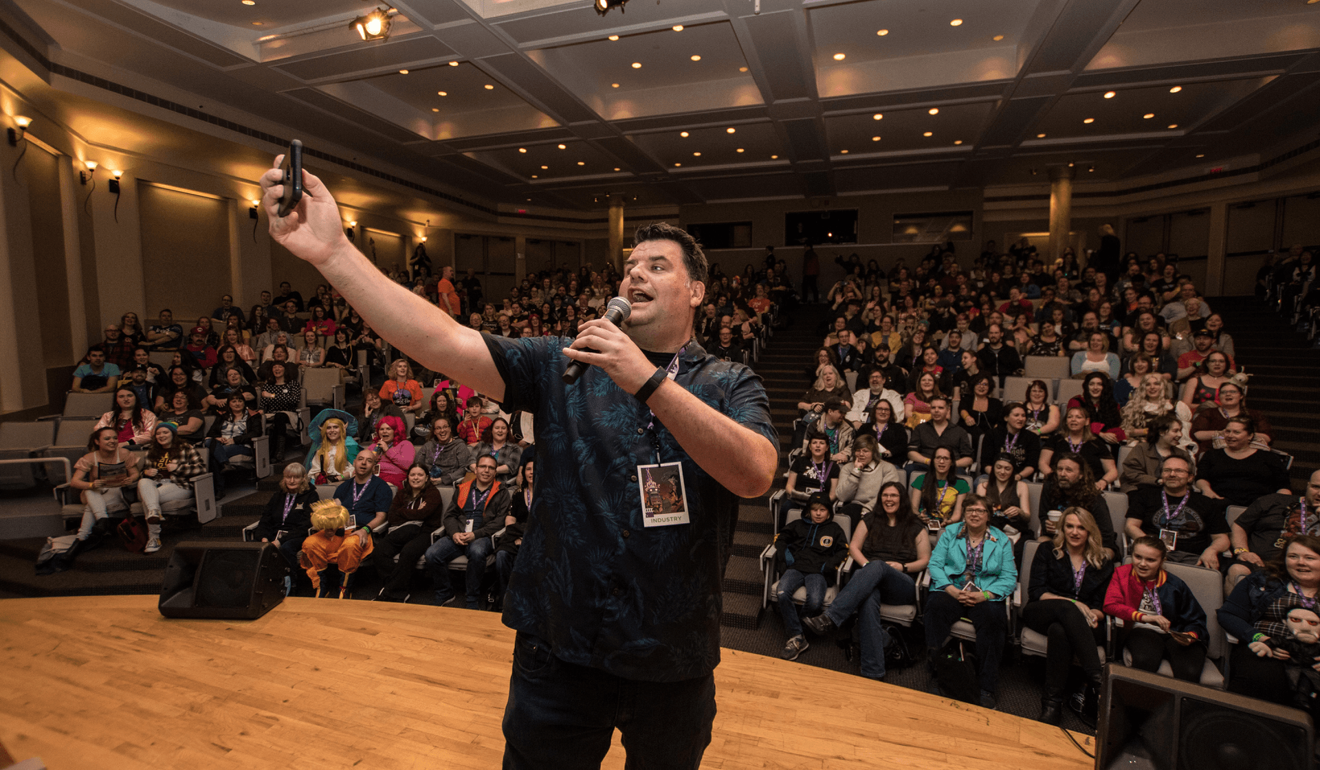 person talking into a microphone taking a selfie with a crowd behind him