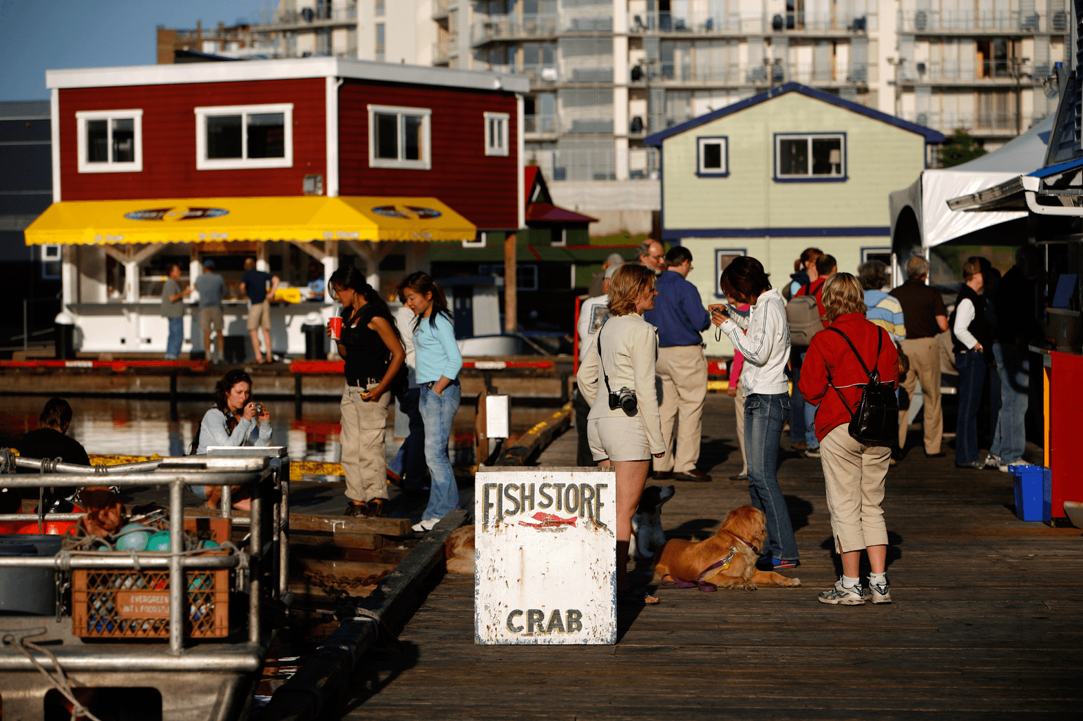 a bunch of people walking on a wharf outside a fish store