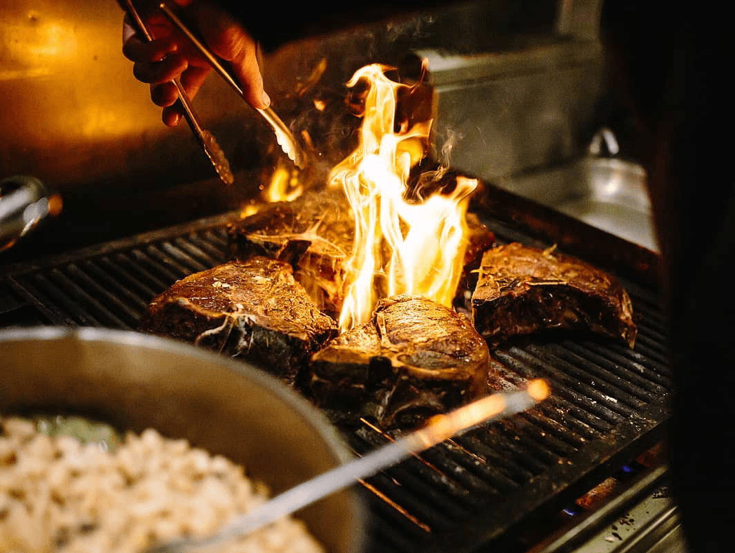 steaks cooking on the grill with flames