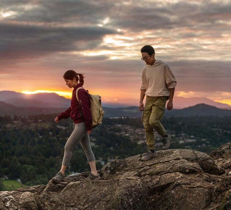 Two people hike along a ridgeline at sunset in Victoria, BC
